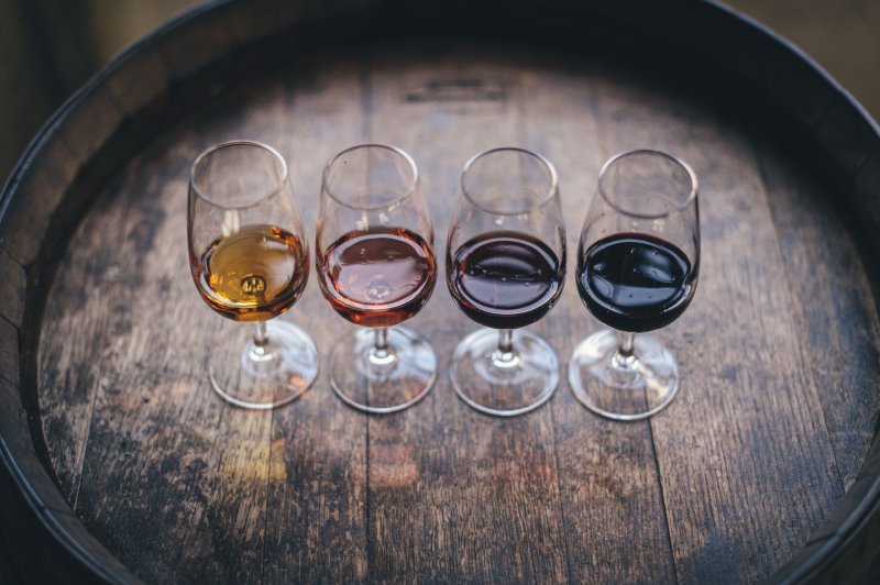 Vier Weingläser mit unterschiedlichen Weinen stehen in einer Reihe auf einem Weinfass