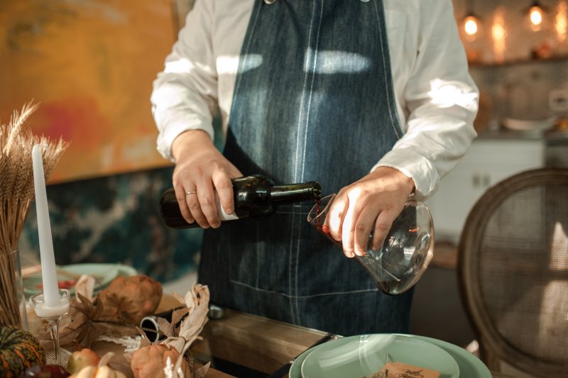 Ein Herr mit Schürze füllt Rotwein von der Flasche in einen Weindekanter